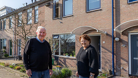 Op de foto staan een man en een vrouw naast elkaar voor een huis.