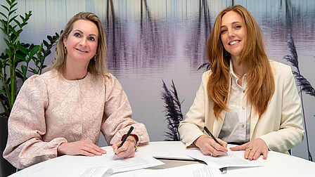 Op de foto ondertekenen twee vrouwen met een pen twee papieren.