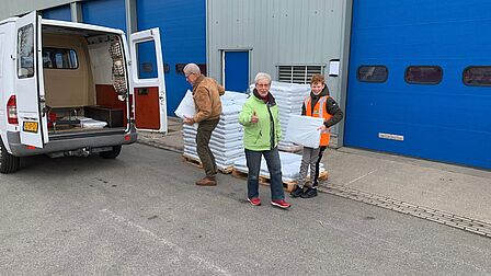 Op de foto staat een bestelbus voor een bedrijfspand, waar drie mensen met zakken compost in hun handen staan.