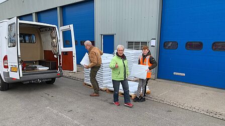 Op de foto staat een bestelbus voor een bedrijfspand, waar drie mensen met zakken compost in hun handen staan.