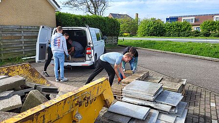Op de foto ziet u inwoners die tuintegels in een afvalcontainer leggen