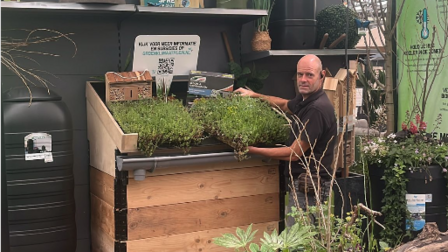 Op de foto is een man te zien die een plantenbak vasthoudt. Om hem zien zijn meerdere plantenbakken te zien.