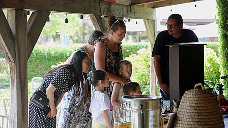 Op de foto staat een imker te praten tegen een gezin bij een bijenkast over de bij